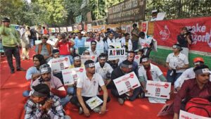 Protesters in India to make Amazon pay. Holding signs against red backdrop.